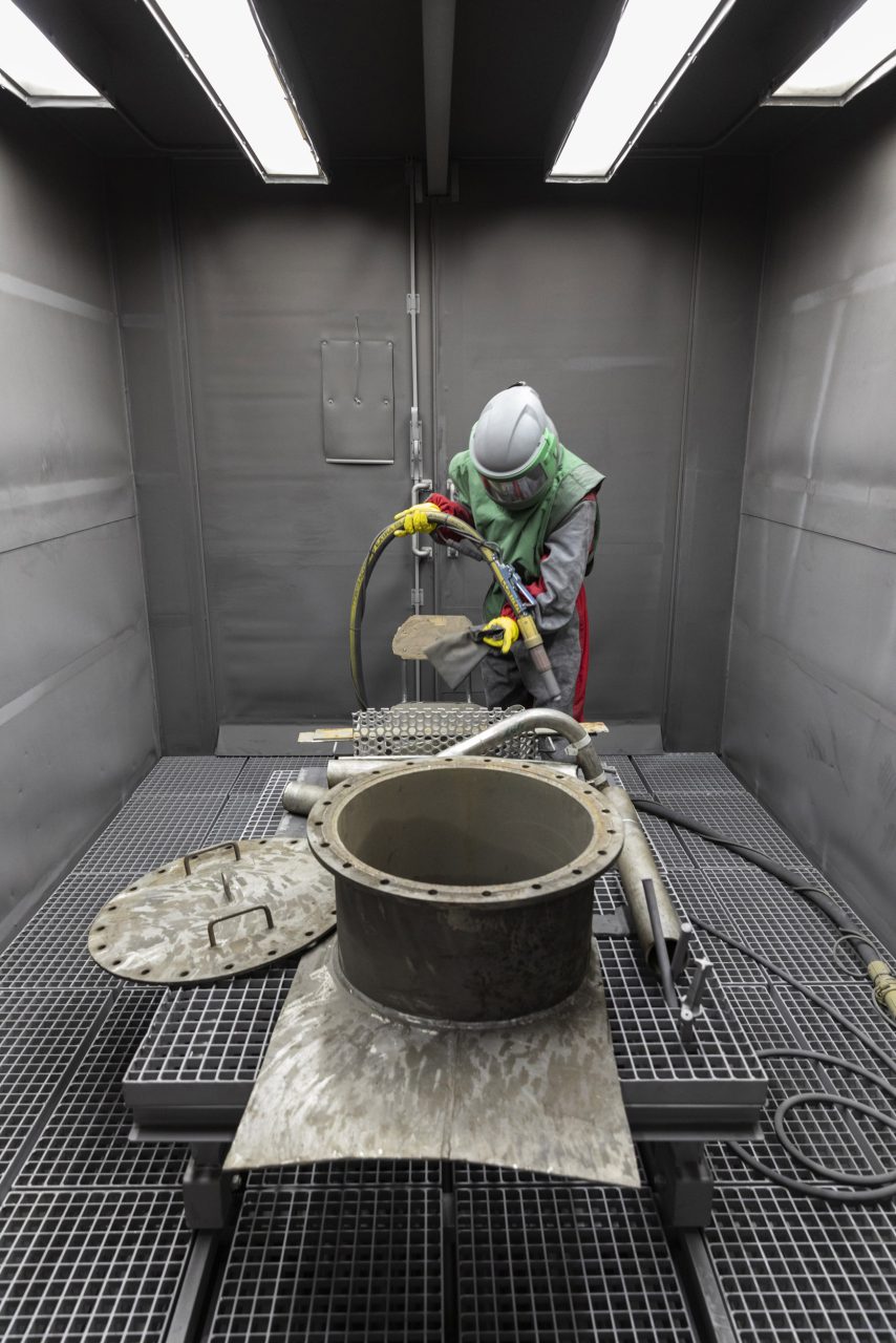 Photo industrielle de portrait métier d'un grenailleur industriel au travail dans une cabine de grenaillage